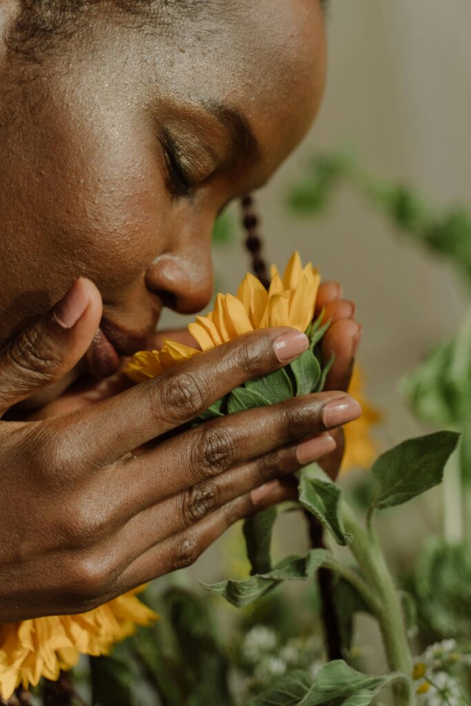 Close-up image of a woman with eyes closed, enjoying the scent of a sunflower indoors.